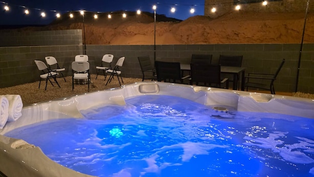 Un bain à remous avec un éclairage bleu, entouré de chaises et bordé d’un mur en briques.
