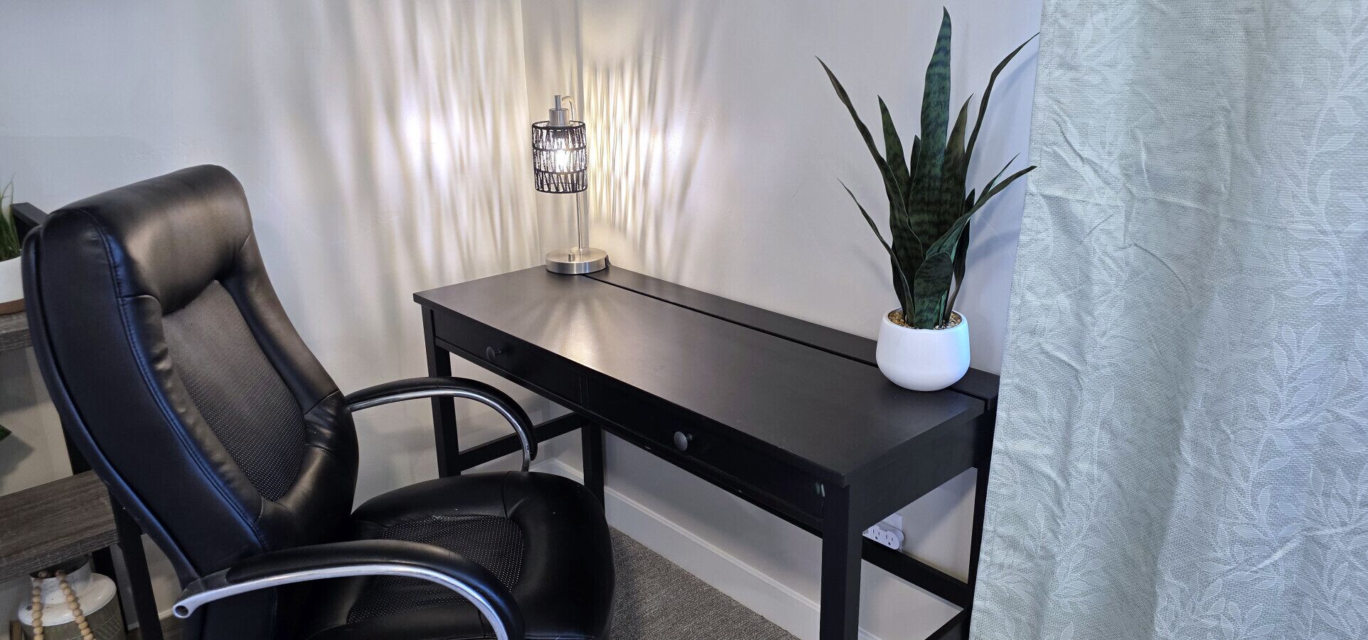 A modern office chair, a black desk, and a potted plant.