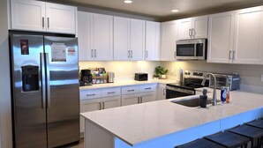 Une cuisine moderne dotée d’appareils électroménagers en acier inoxydable, de meubles blancs, d’un grand îlot central avec des tabourets et d’un four à micro-ondes encastré.