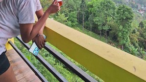 A person on a balcony with a view of a green valley and distant hills. - Nambang Homestay Tinchuley (Darjeeling)