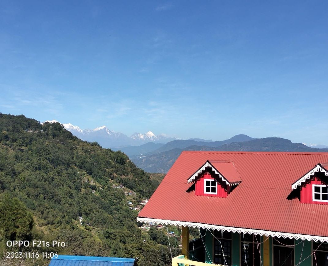 Un edificio con tetto rosso, rivestito di bianco, e una piccola finestra, circondato da dolci colline verdi e montagne lontane.
