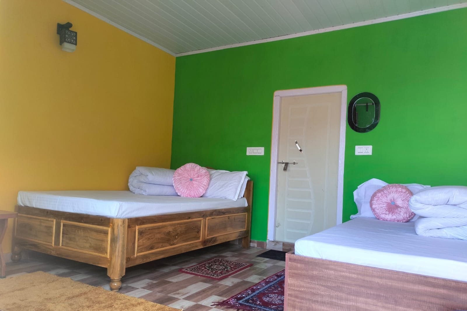 A room with two beds, a wooden cabinet, a green wall, and a white door.