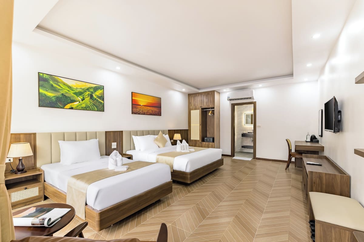 A hotel room with two beds, a desk, a chair, a TV, and artwork on the walls.
