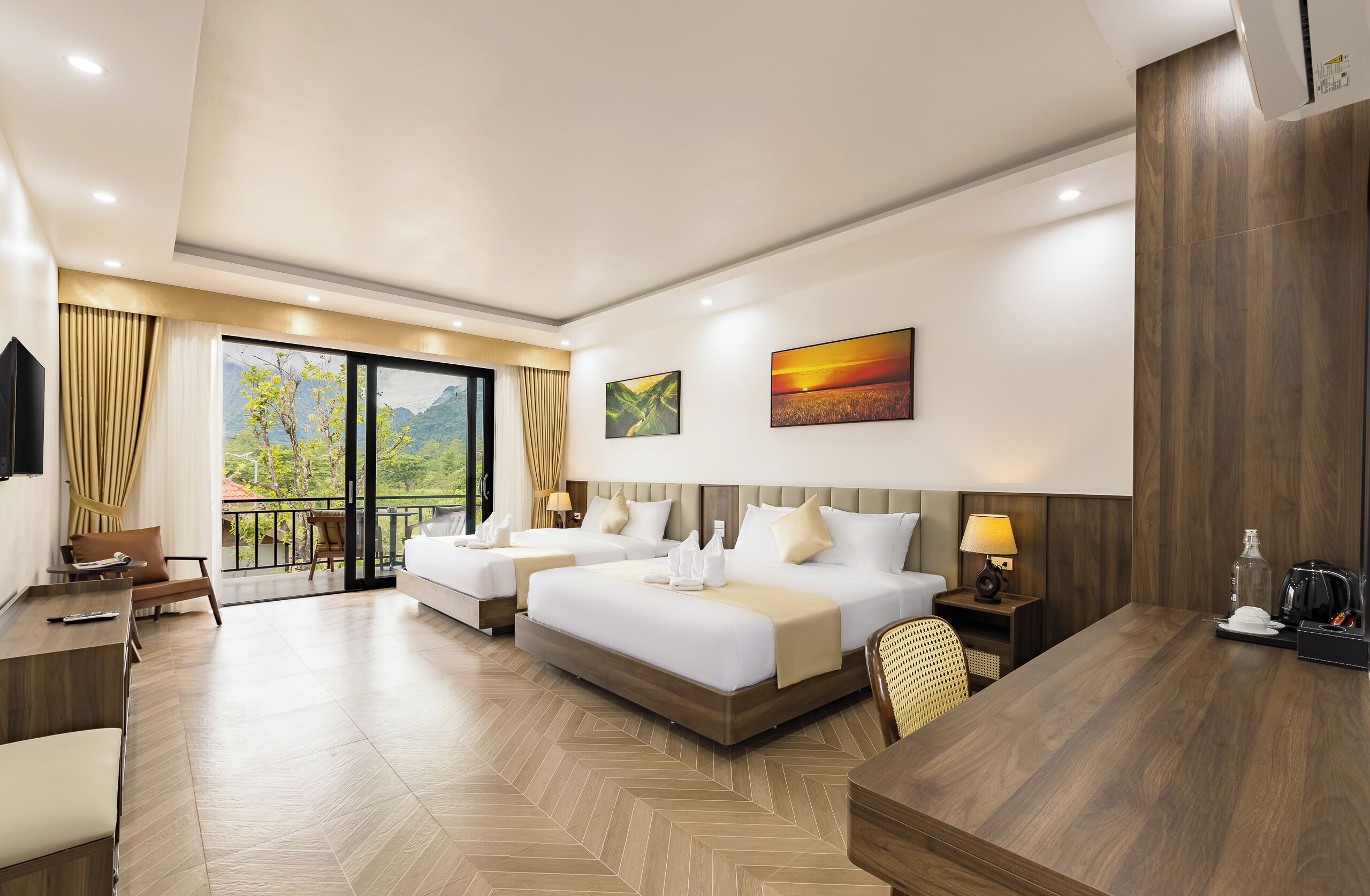 A hotel room with two beds, a desk, a chair, a TV, and a balcony with a view of mountains.