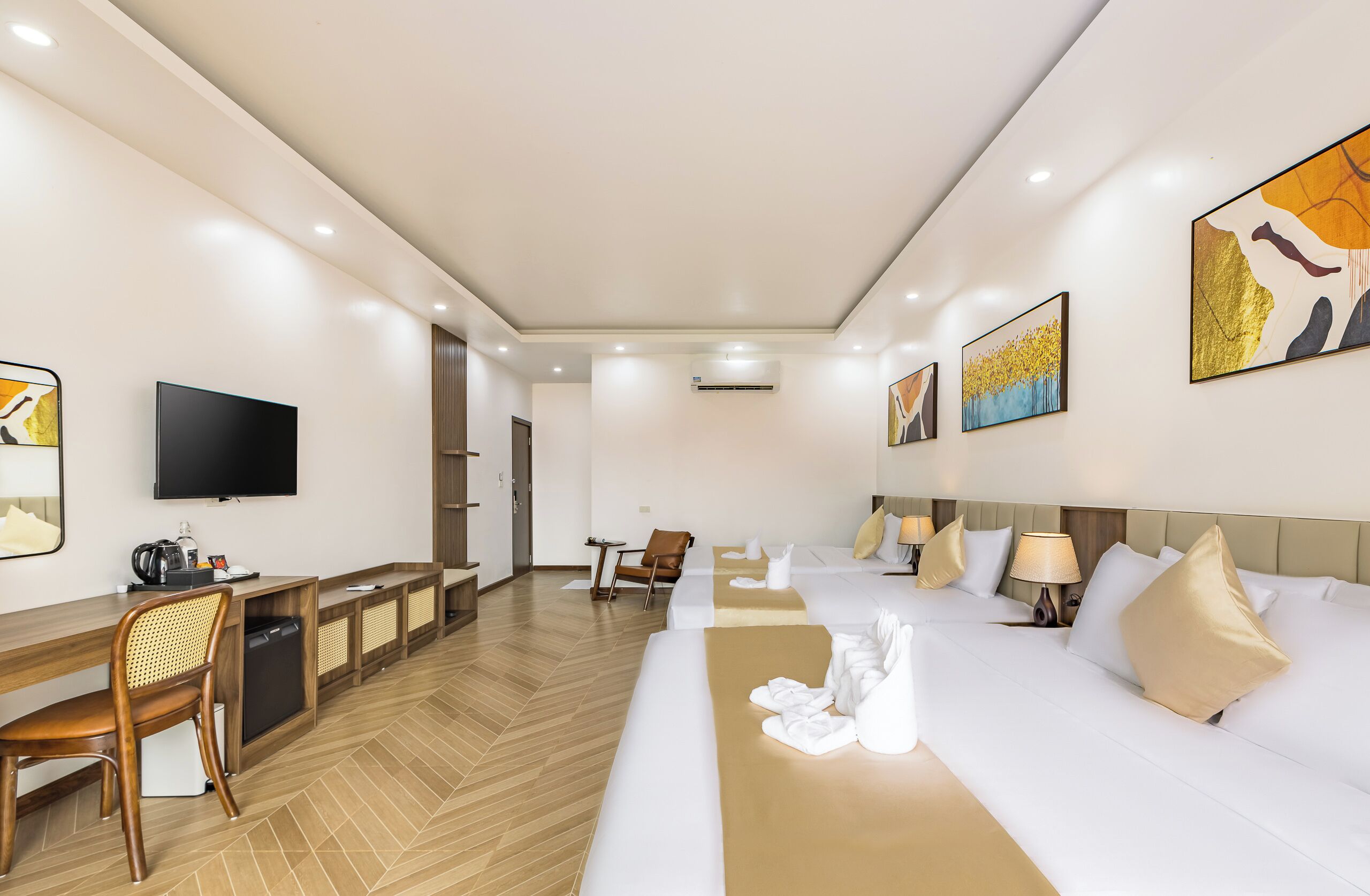 A hotel room with a large bed, a desk with a chair, a television, and artwork on the walls.