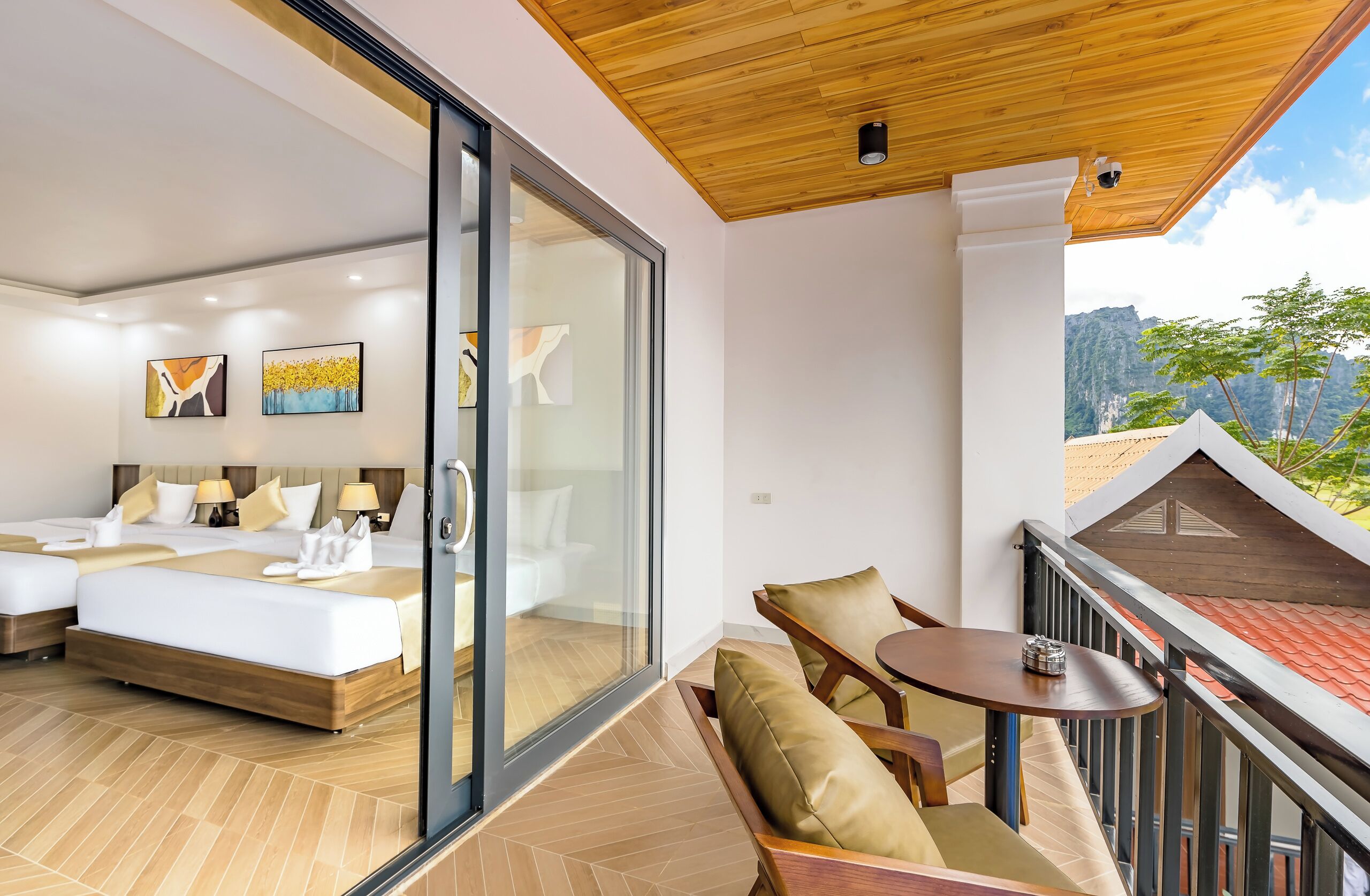 Una habitación de hotel moderna con una cama grande, dos mesitas de noche y un ventanal que da a un balcón con vistas a las montañas.