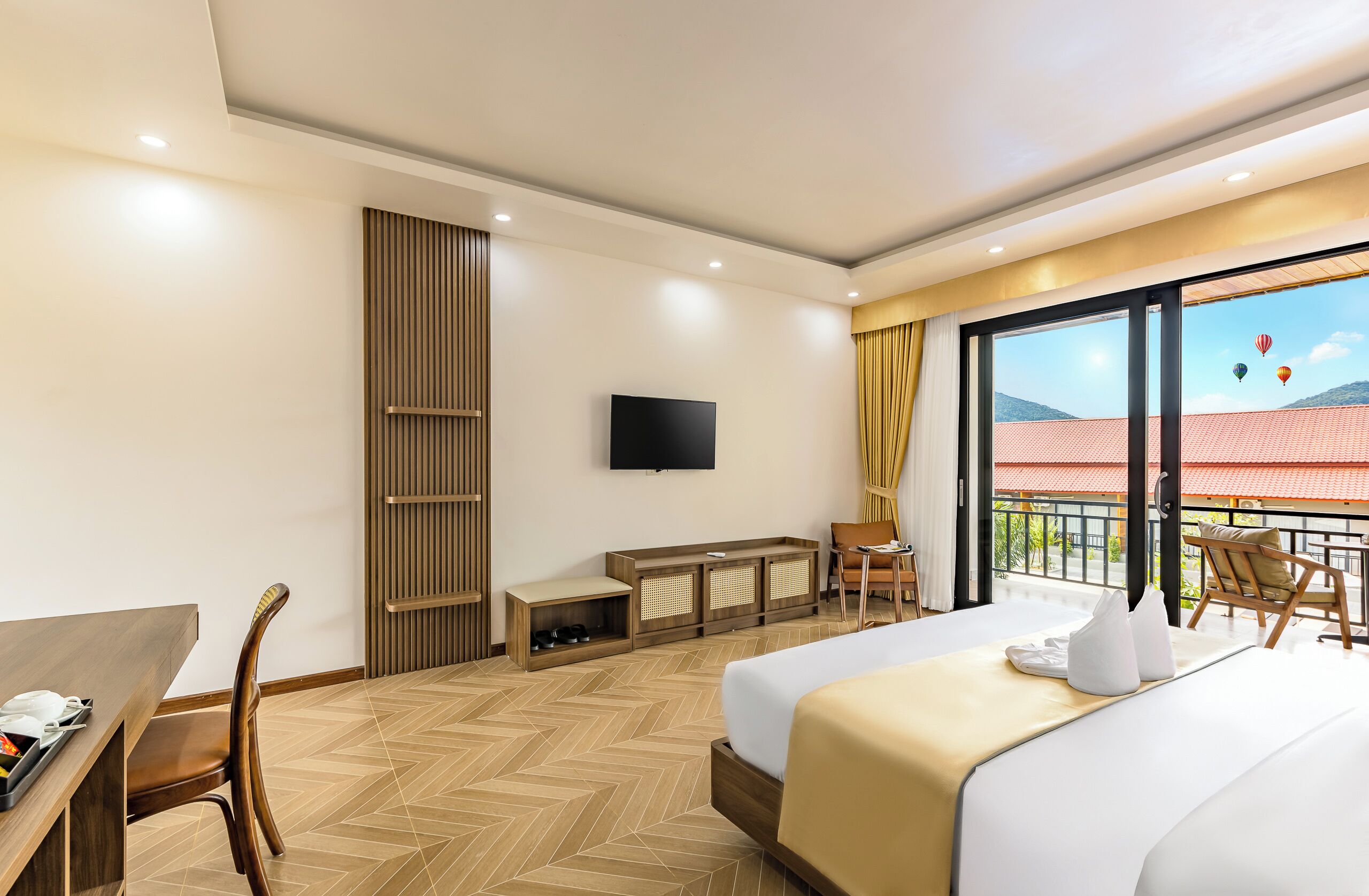 Camera d'albergo con un letto, una scrivania, una sedia, una TV e un balcone con vista sulla città.
