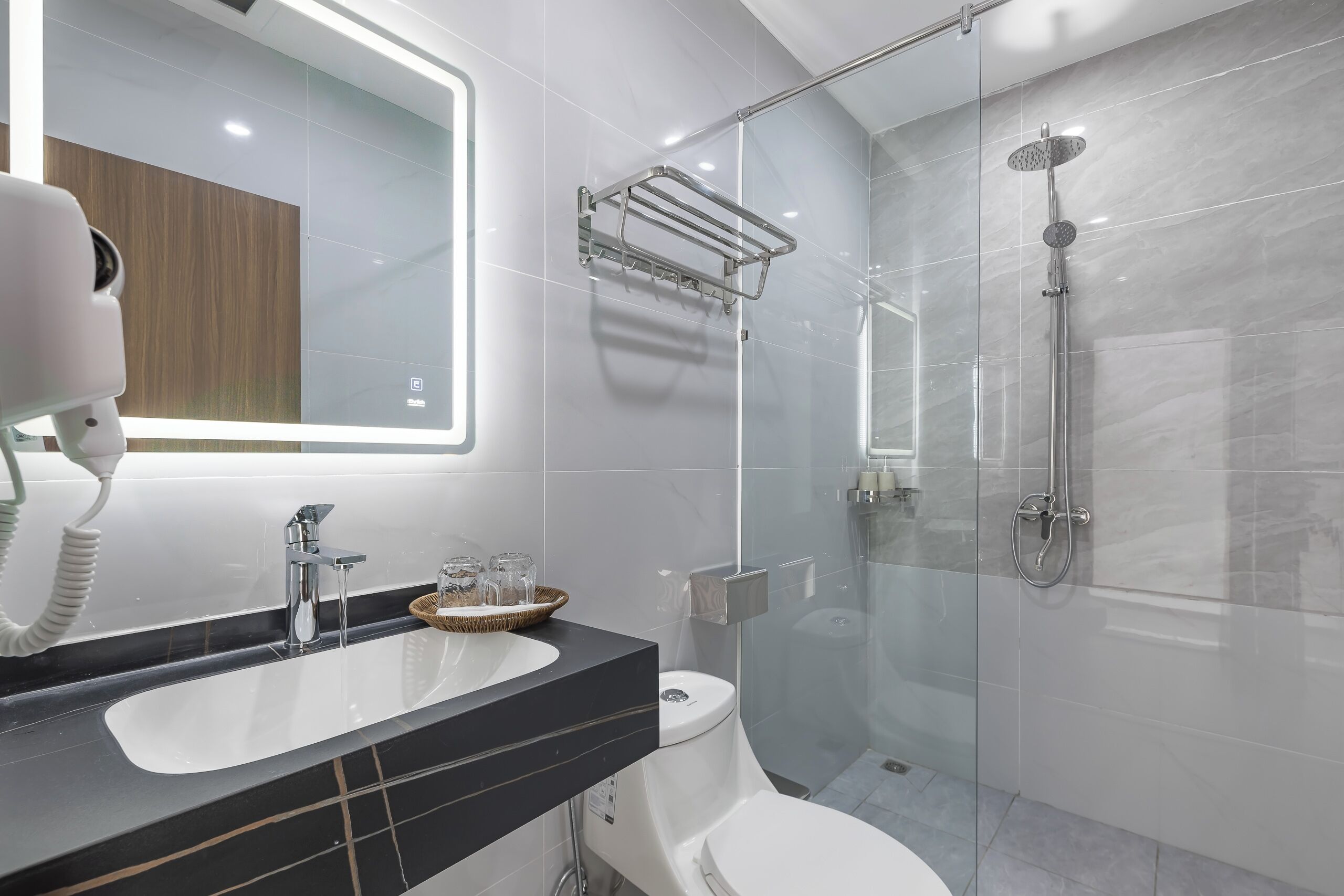 Un baño moderno con ducha envuelta en vidrio, inodoro blanco y tocador con encimera negra.