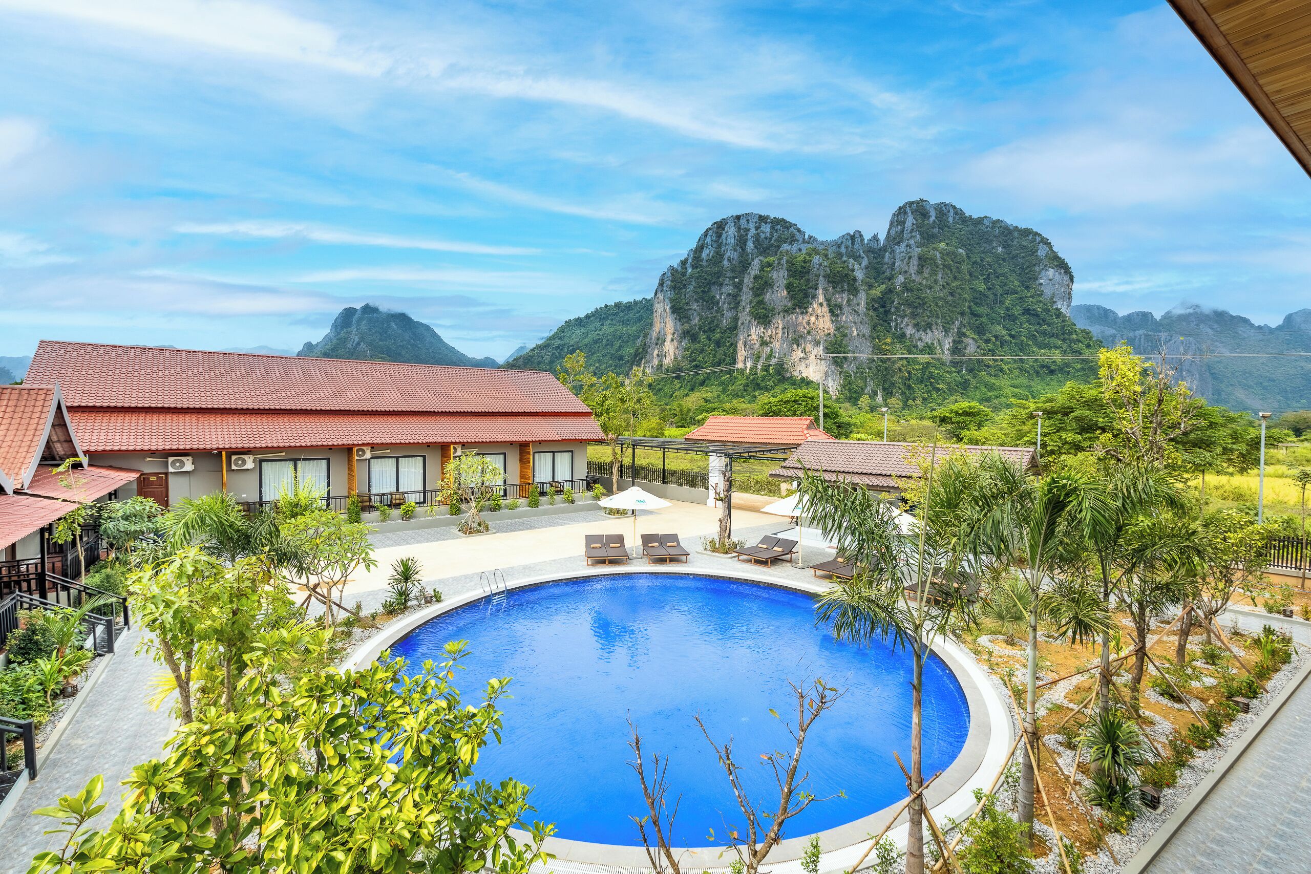 A hotel with a swimming pool surrounded by greenery and a view of a mountainous landscape.