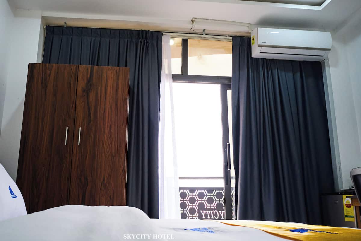 Habitación de hotel con cama, armario, ventana con cortinas y aire acondicionado.