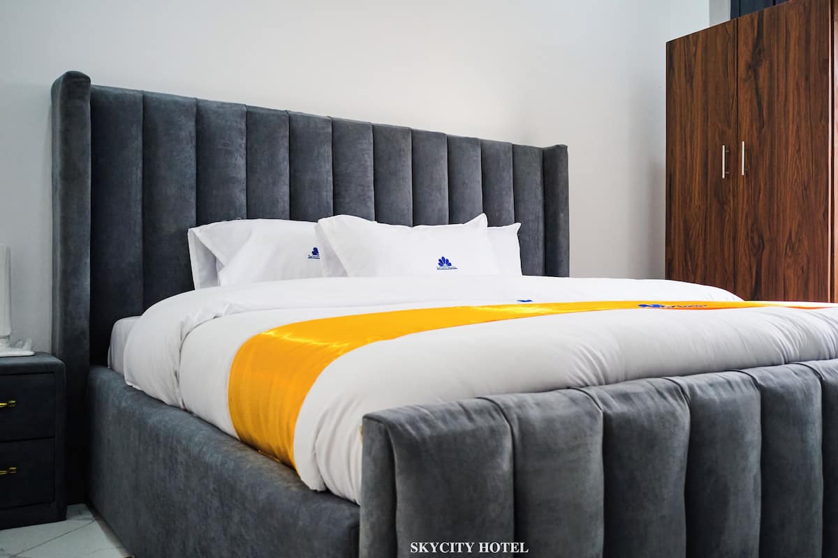 Un dormitorio moderno con una cama grande, cabecera tapizada en gris, ropa de cama blanca y un armario de madera.