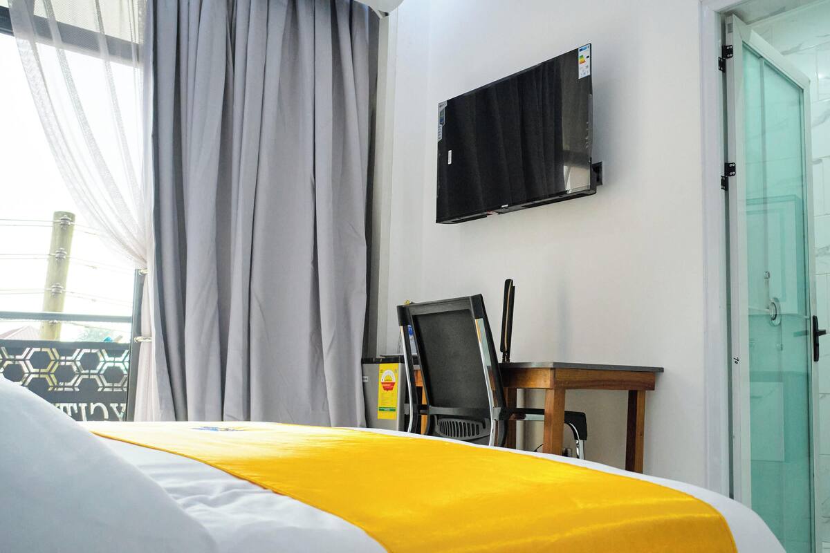 Habitación de hotel con cama, escritorio, silla, televisor y puerta de ducha de vidrio.