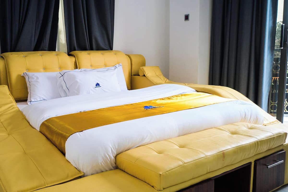 Habitación de hotel con una cama grande, cabecera tapizada de color amarillo, ropa de cama blanca y vistas de la ciudad a través de la ventana.