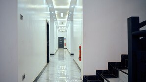A hotel hallway with a modern design, featuring a long corridor with a marble floor, a staircase on the right, and a door at the end. - Skycity Hotel Gh (Amrahia)