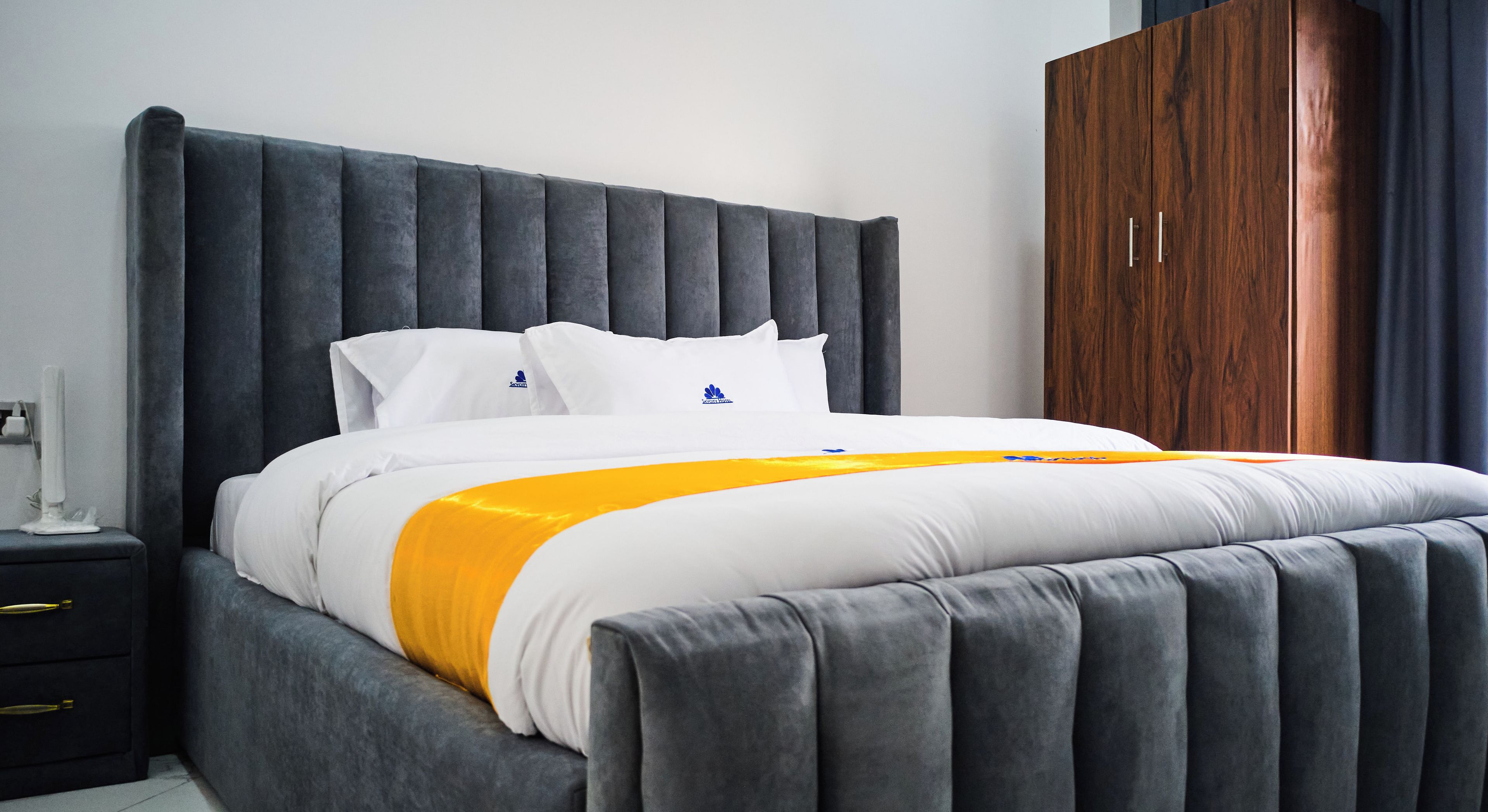 Quarto moderno com uma cama grande, cabeceira estofada cinza, roupa de cama branca e um guarda-roupa de madeira.