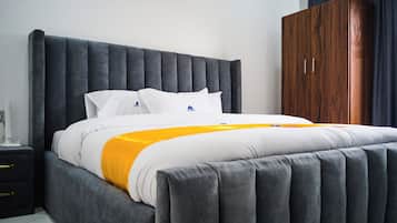 Quarto moderno com uma cama grande, cabeceira estofada cinza, roupa de cama branca e um guarda-roupa de madeira.