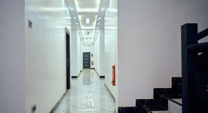 A hotel hallway with a modern design, featuring a long corridor with a marble floor, a staircase on the right, and a door at the end. - Skycity Hotel Gh (Amrahia)
