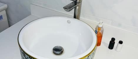 A bathroom with a mosaic-tiled sink, a modern faucet, and a white countertop.