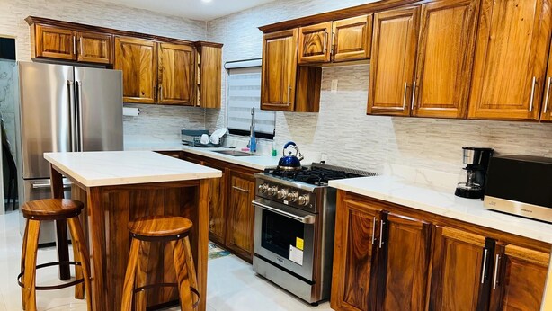 A modern kitchen with wooden cabinets, a stainless steel refrigerator, a gas stove, and a built-in oven. - Jebucks Escape (Portmore)