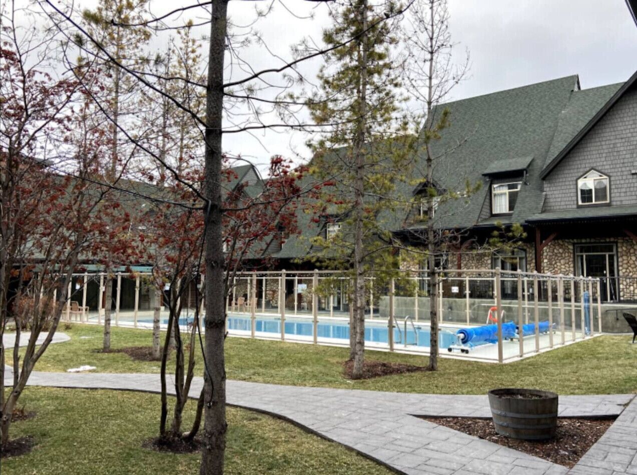 Un immeuble résidentiel doté d’une piscine, entouré d’arbres et bordé d’une allée pavée.