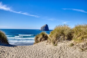 Une plage de sable avec des dunes herbeuses et une grande formation rocheuse dans l’océan.