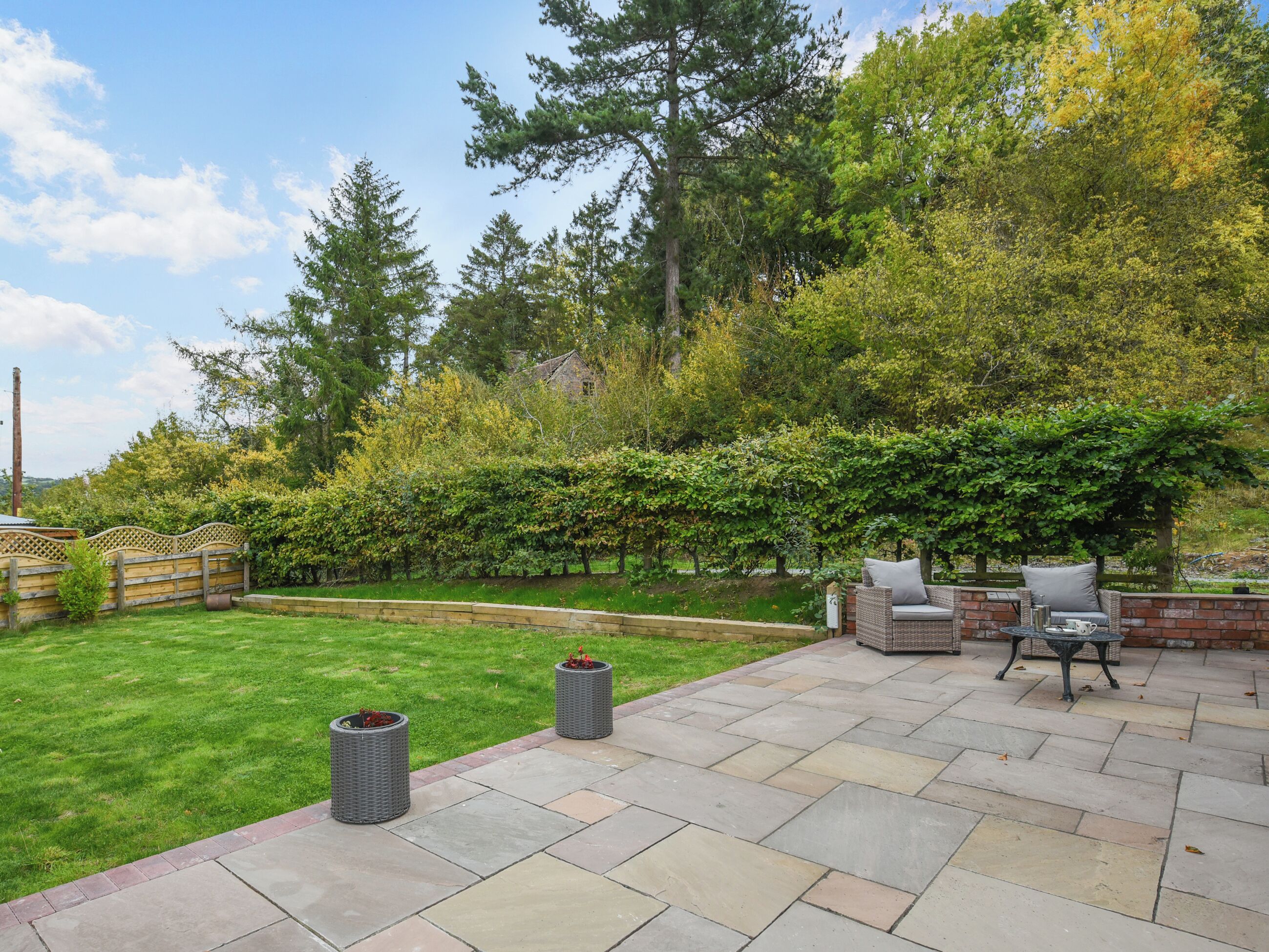 Eine Terrasse mit Gartenmöbeln, einem gepflegten Rasen und einer Hecke.