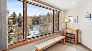 Ein Zimmer mit einem großen Fenster, einer hölzernen Bank, einer Lampe und einem an der Wand befestigten Regal.