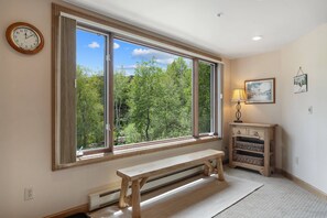 Ein Zimmer mit einem großen Fenster, einer Bank, einer Lampe und einer Wanduhr.
