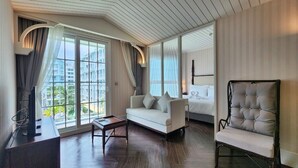 A modern hotel room with a large window, a white sofa, a tufted armchair, and a wooden coffee table. - Grand Florida 1Bedroom CloseToBeach G410 (Sattahip)