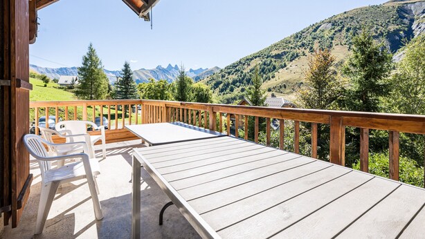 A wooden deck with a table and chairs, overlooking a mountainous landscape.