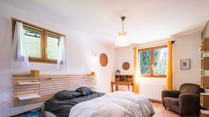 A bedroom with a bed, bedside table, chair, and a window with curtains.