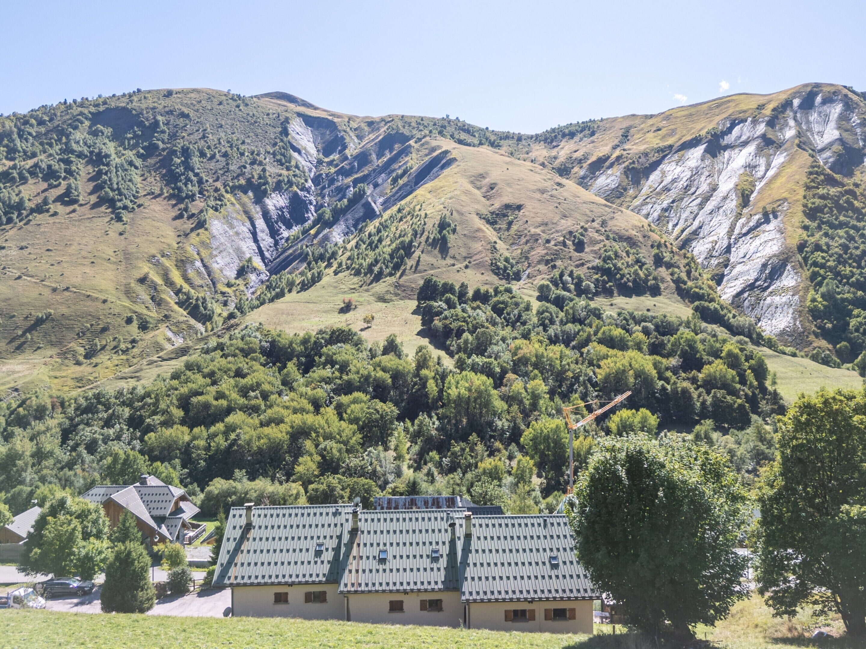 A building with a sloped roof and multiple windows, surrounded by lush green hills and a clear sky.