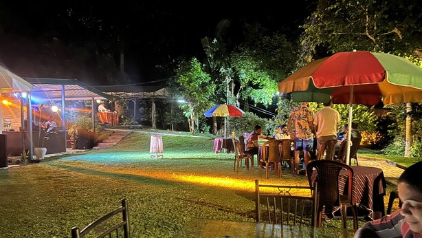 An outdoor dining area with tables and chairs, surrounded by greenery and illuminated by ambient lighting. - Thomasz Lodge (Kandy)