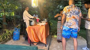 An outdoor dining area with a table covered by an orange cloth, a gas cylinder, and a hanging light fixture. - Thomasz Lodge (Kandy)