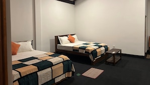 A room with two beds, each with a different patterned bedspread. There is a small wooden table and a red and green striped rug on the floor. - Thomasz Lodge (Kandy)