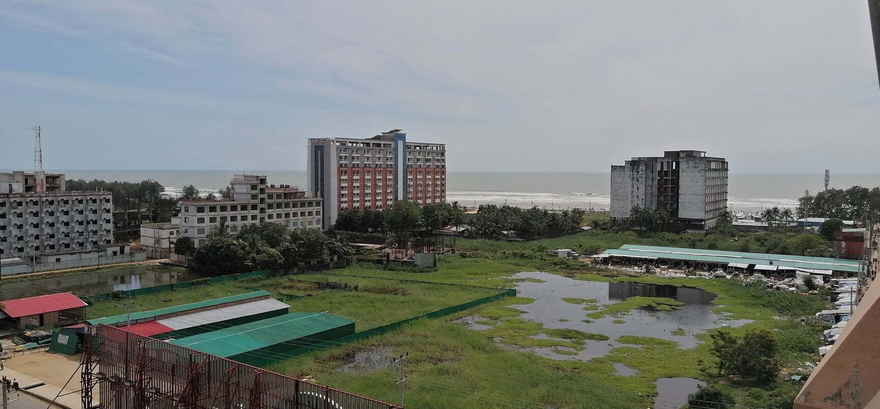 A coastal view with a large building, a smaller structure, and a green area with water.