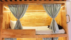 Ein Holzbett mit Etagen und Vorhängen, die an der Oberseite gebunden sind, ein Holz-Kopfteil und ein Metallgriff auf der rechten Seite.