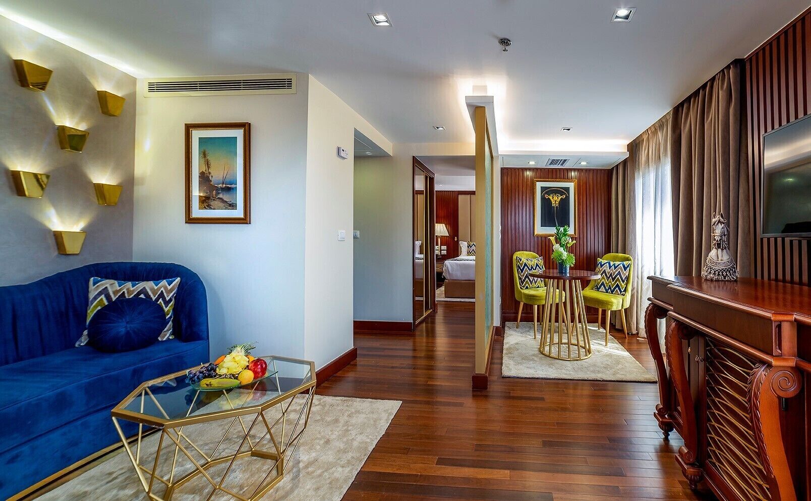 A modern living room with a blue sofa, a glass coffee table, and a dining area with yellow chairs.