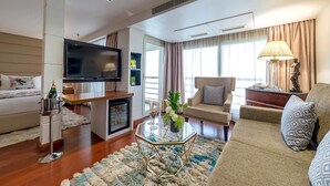 A modern living room with a flat-screen TV, a glass coffee table, a sofa, a chair, and a small refrigerator. - Sonesta Sun Goddess Nile cruise ship - 4 & 7 nights - From Luxor every Monday (Luxor)