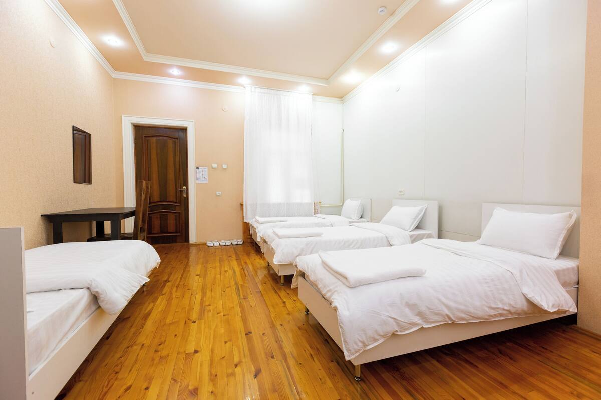 A hotel room with wooden flooring, white beds, a wooden door, and a small table.