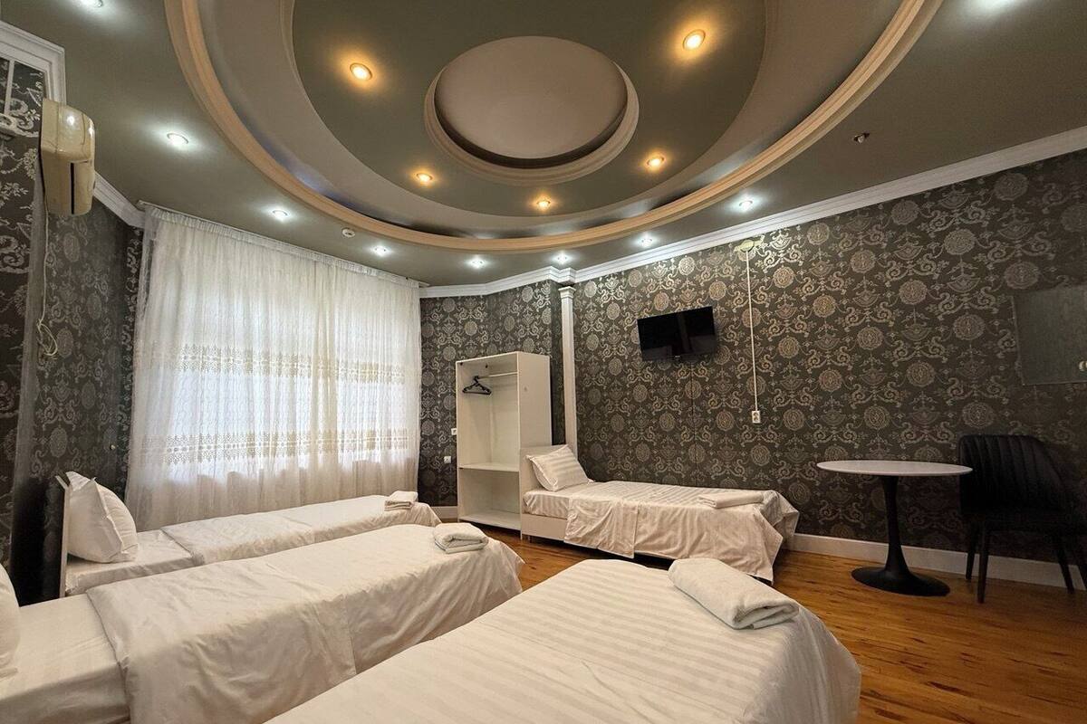 A hotel room with four single beds, a wardrobe, a small table, and a TV mounted on the wall.