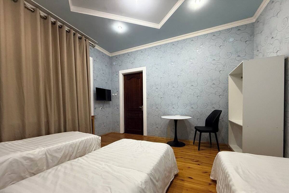 A hotel room with two beds, a small table, a chair, a TV, and a wardrobe.