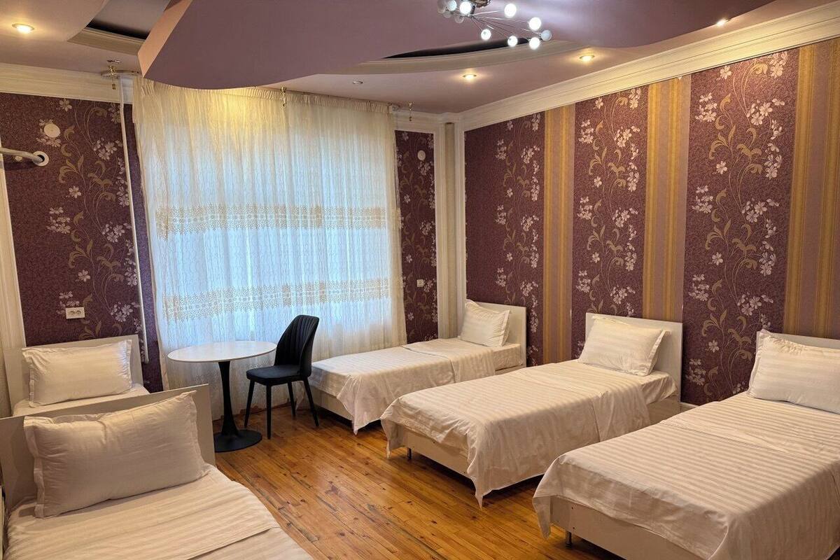 A hotel room with four single beds, a small round table, and a chair.