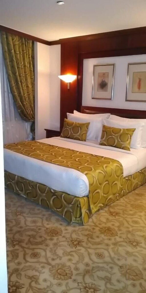 A hotel room with a bed, a nightstand, a wall-mounted lamp, and framed pictures on the wall.