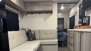 A compact RV interior with a sofa, kitchenette, and storage cabinets. - Moonlite Wolf RV: King, Bunks, Fire Pit & Outdoor! (Spring Branch)