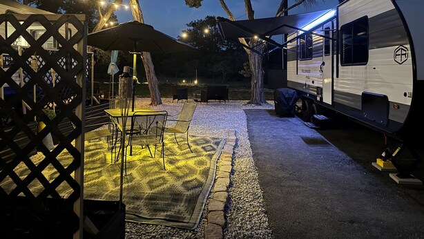 A campsite with a covered dining area, outdoor seating, and a trailer. - Moonlite Wolf RV: King, Bunks, Fire Pit & Outdoor! (Spring Branch)