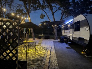 A campsite with a covered dining area, outdoor seating, and a trailer. - Moonlite Wolf RV: King, Bunks, Fire Pit & Outdoor! (Spring Branch)