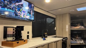 A modern kitchen with a flat-screen TV, coffee maker, and a wooden cabinet. - Moonlite Wolf RV: King, Bunks, Fire Pit & Outdoor! (Spring Branch)