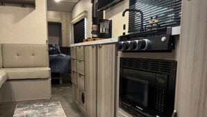A compact RV kitchen with a built-in oven, microwave, and a small coffee maker. - Moonlite Wolf RV: King, Bunks, Fire Pit & Outdoor! (Spring Branch)