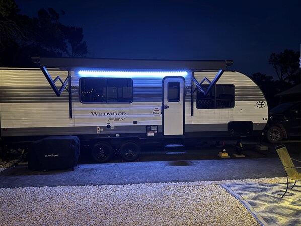 A Wildwood F5X RV with a sliding door, a kitchen area, and a covered outdoor seating space. - Moonlite Wolf RV: King, Bunks, Fire Pit & Outdoor! (Spring Branch)